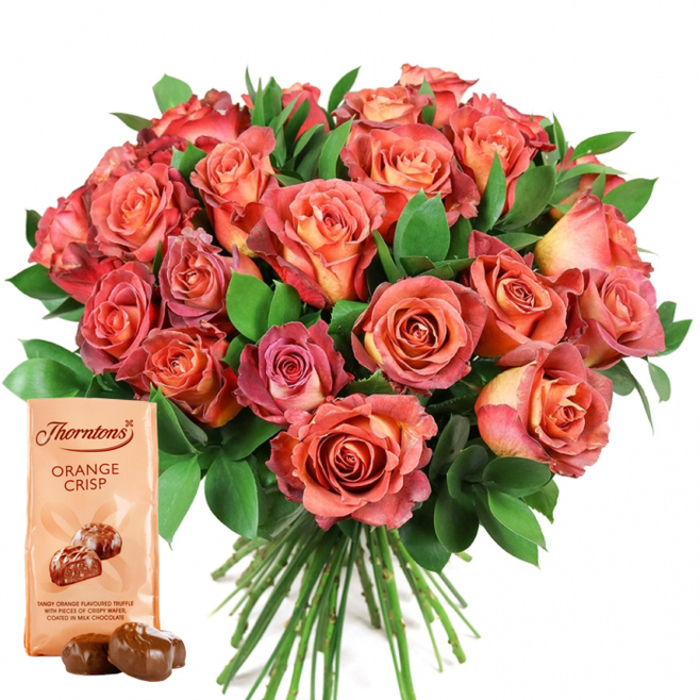 Dominating the scene is a sumptuous hand-tied bouquet of roses, each flower exuding the artistry and freshness Manor House florists are known for. The arrangement is awash in a kaleidoscope of warm and refined shades: central petals glow with delicate peach and buttery cream, while the outlying petals transition seamlessly into lustrous coral, spirited salmon, and deep rosy pinks, some delicately tinged with golden undertones. The lush blossoms are densely clustered, forming a generously rounded bouquet, with glossy, deep green foliage-possibly a mix of eucalyptus and salal-carefully placed to create depth and frame the floral centerpiece. Anchoring the display, a light beige pouch of Thorntons Orange Crisp chocolates leans against the flowers, its packaging echoing the elegance of the bouquet with rich script and enticing images of milk chocolate truffles. The product is described as "Tangy orange flavoured truffle with pieces of crispy wafer, coated in milk chocolate," while two glossy, chocolate-brown truffles, split from the pouch, rest temptingly at the front, their smooth coating catching the light. The bouquet's long green stems are visible beneath the explosion of colour, hinting at meticulous preparation. Set against a pristine, white canvas, the arrangement stands out as a portrait of joyful celebration-perfect for gifting on Valentine's Day, birthdays, anniversaries, or to show appreciation to someone in Manor House, from the busy corridors of Green Lanes to the tree-lined paths of Finsbury Park.